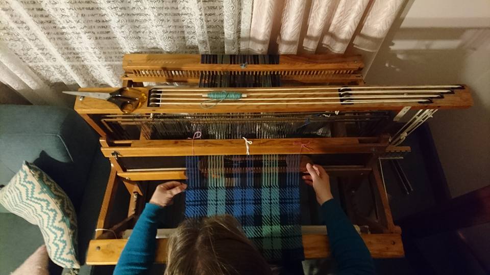 View from above of Emilt weaving blue/green/black twill on a four-shaft table loom using a boat shuttle.